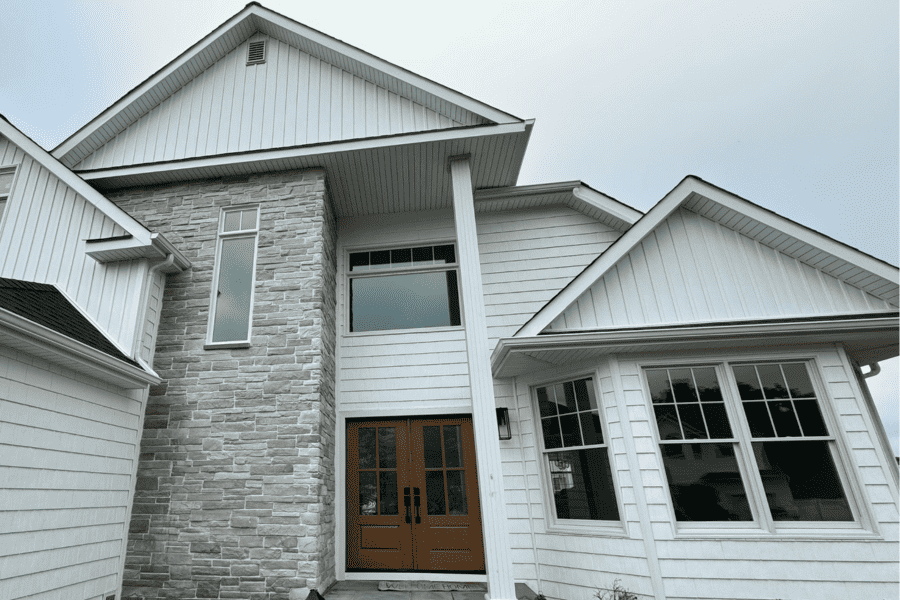 Front view of a modern house with white siding and stone accents, featuring a pair of double doors and large windows under a gray sky.