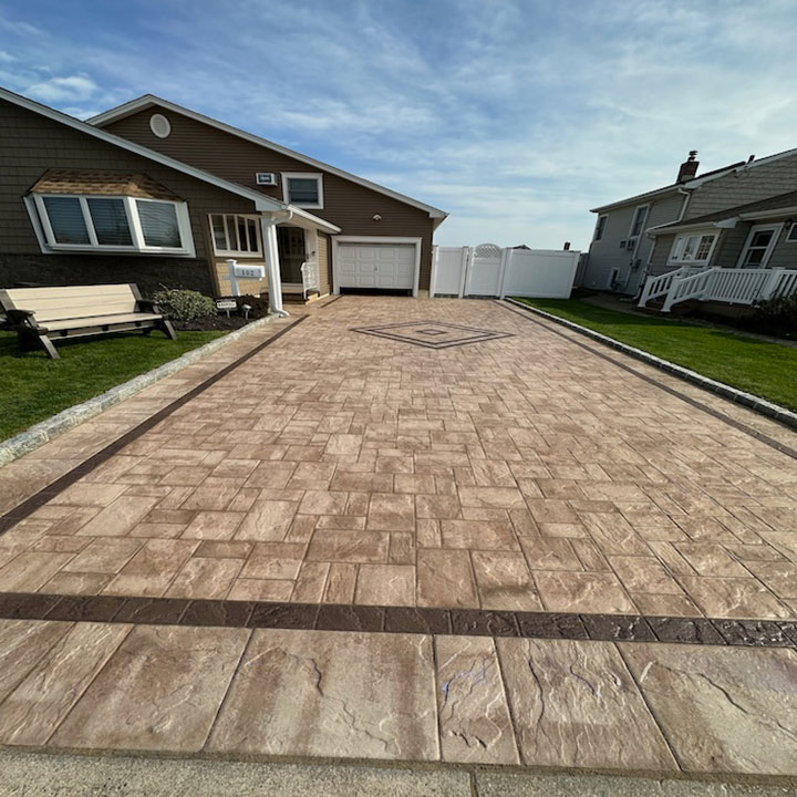A stamped concrete driveway leading to a suburban house with a garage and a small lawn to the left.