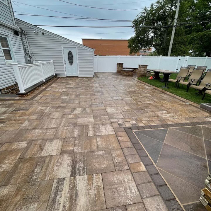 Paved backyard with patterned tiles, featuring patio furniture, a white shed, and surrounding fences under an overcast sky.