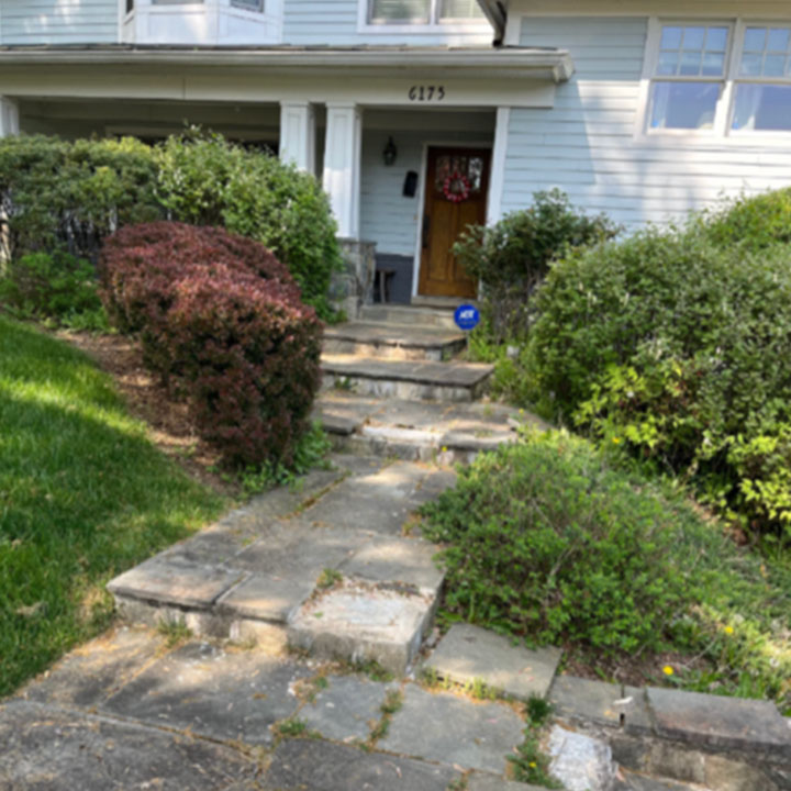 A front yard with an overgrown garden and a stone walkway leading to a house's entrance, displaying the house number 6175.