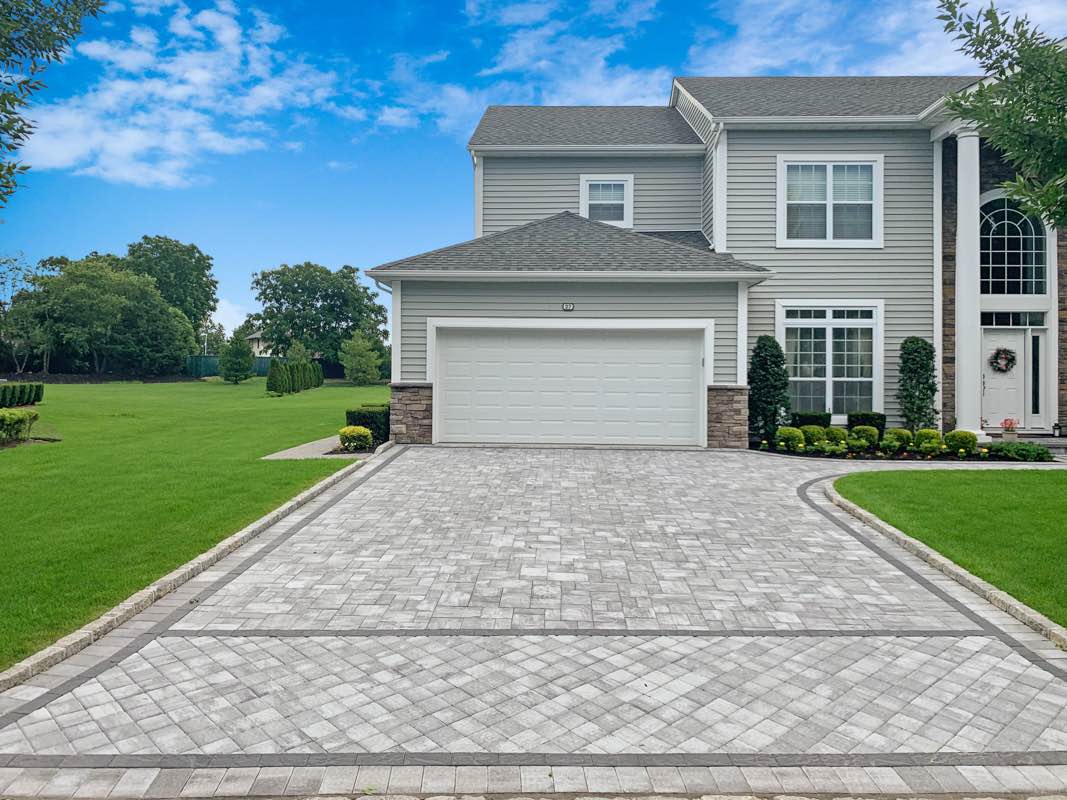 A two-story suburban house with a large driveway and neatly landscaped lawn under a clear blue sky.