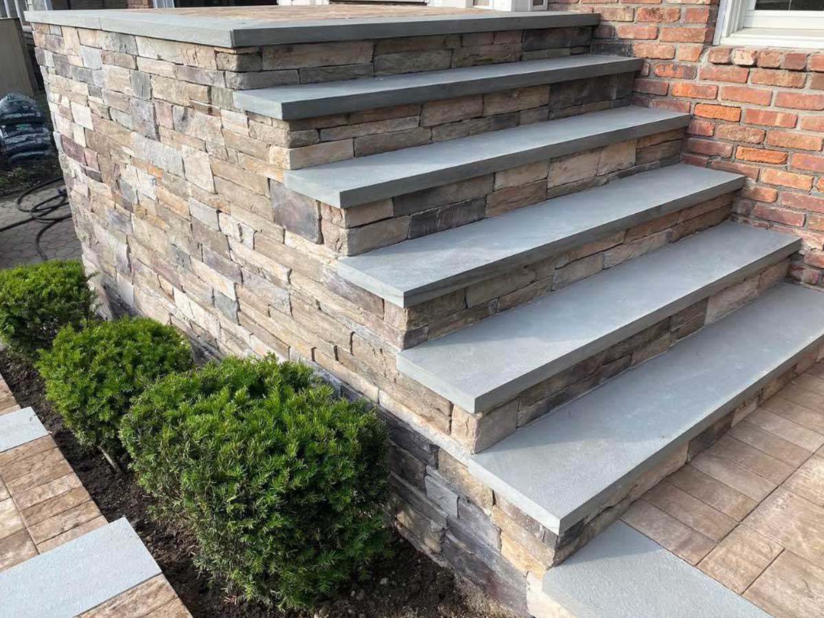 Stone steps with gray treads leading to a brick building, flanked by small green shrubs.