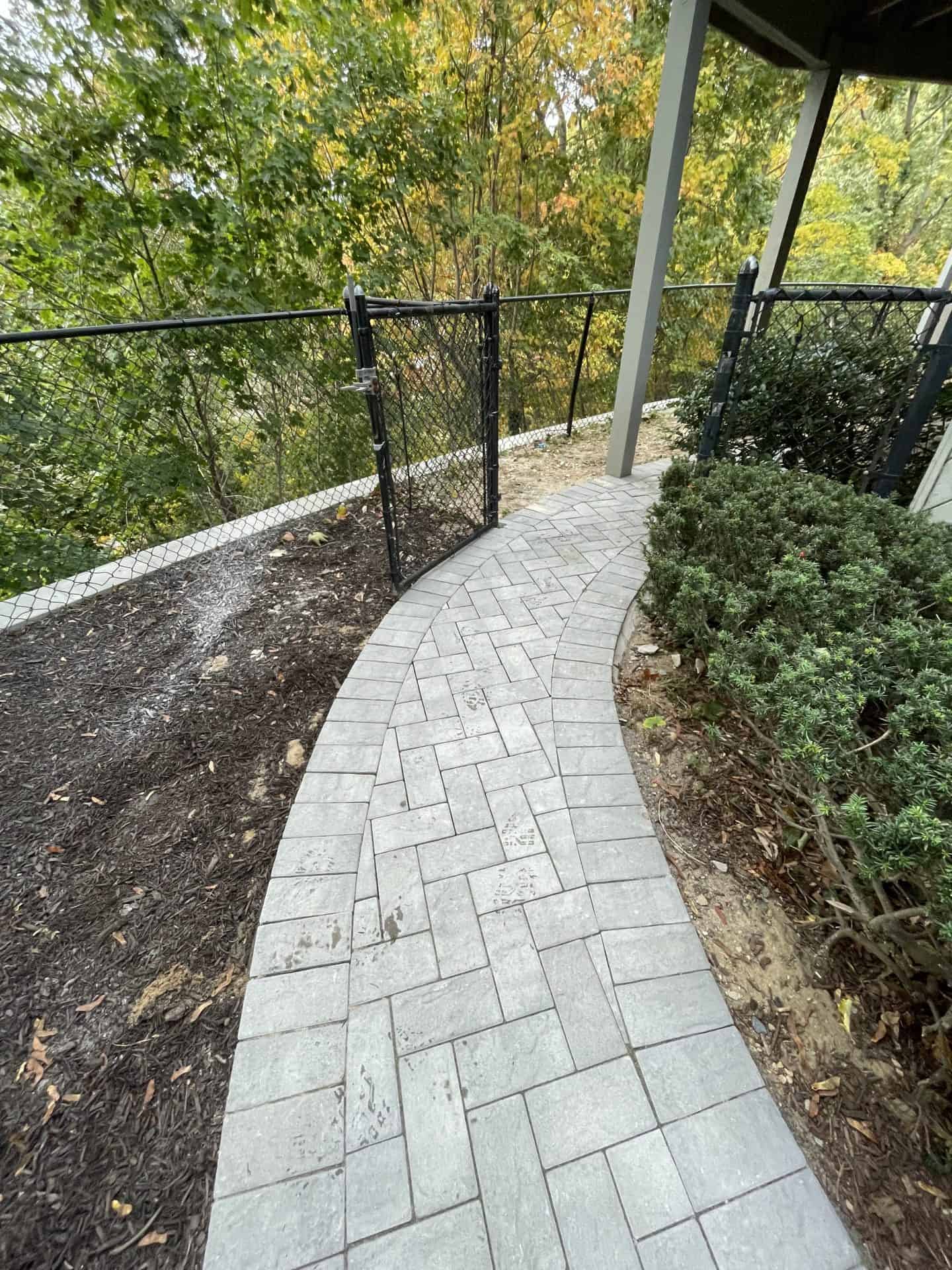 Curved stone pathway leading to a black metal gate, surrounded by greenery and mulch.