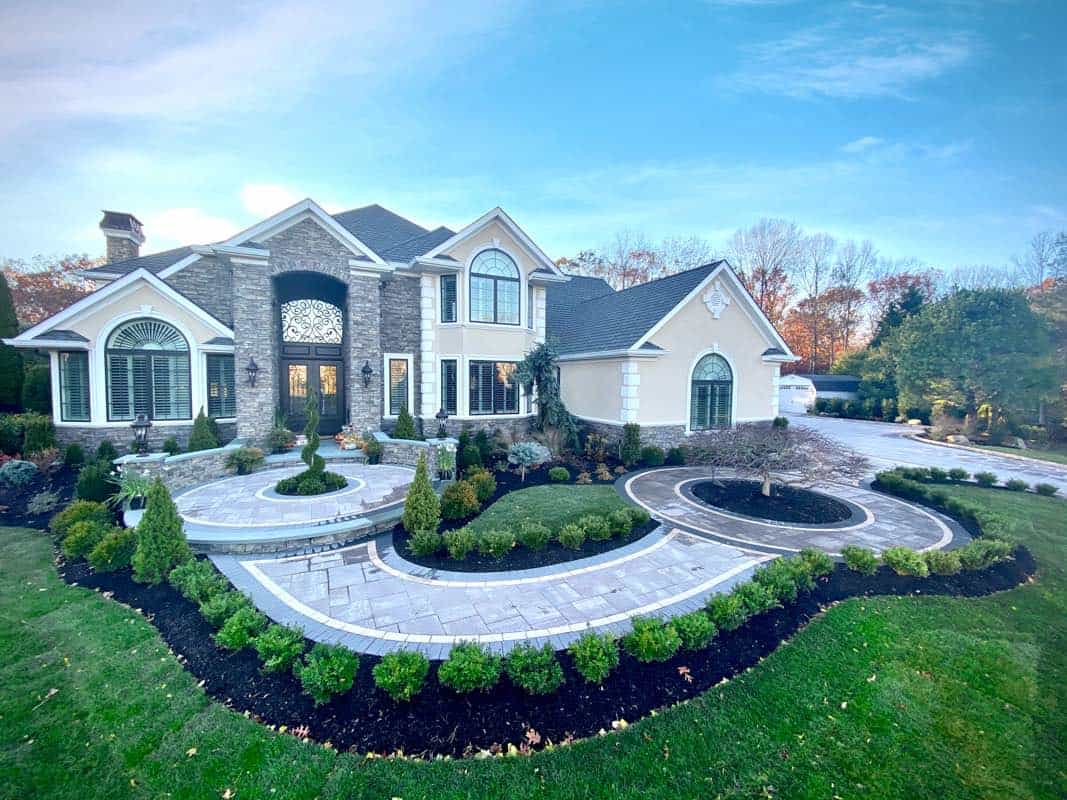 Luxurious house with stone and stucco exterior, arched windows, and manicured landscaping, featuring circular pathways and a driveway.