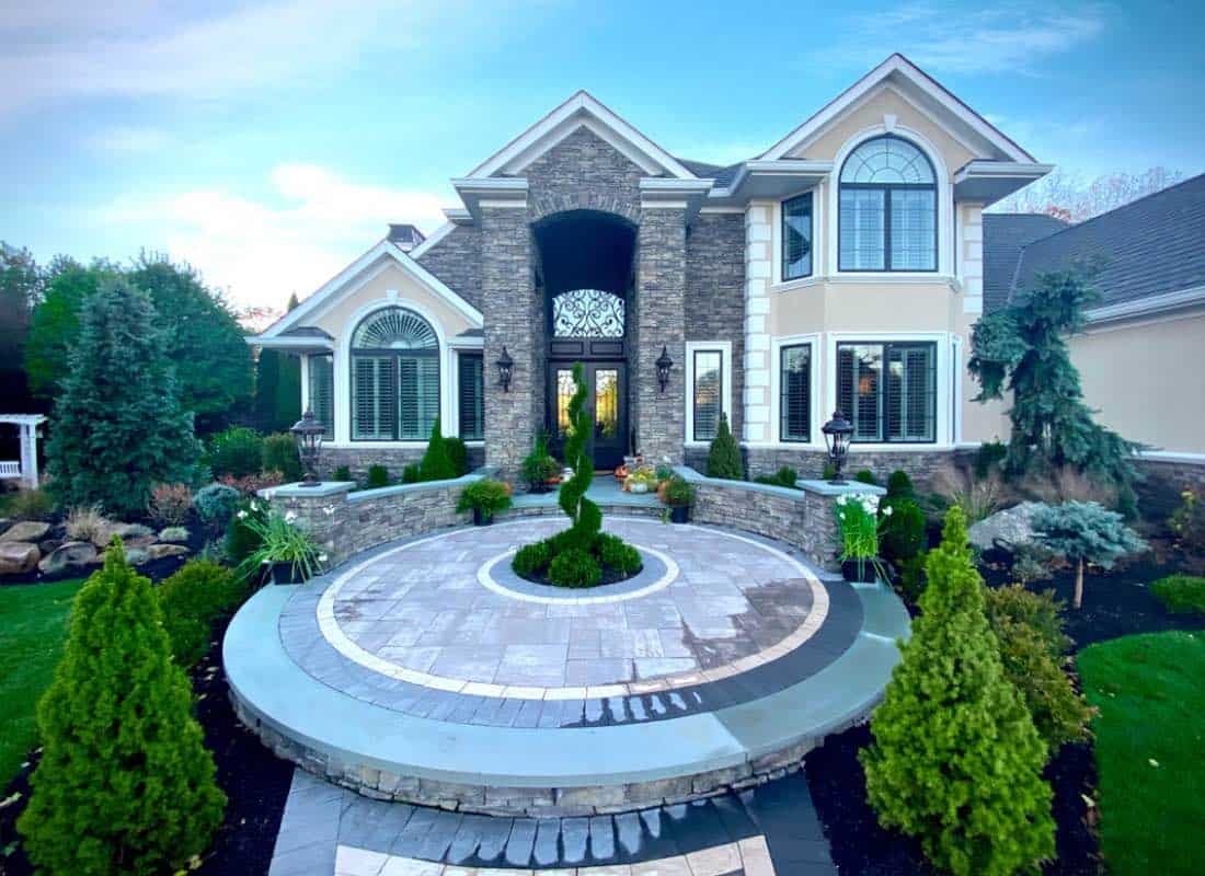 Elegant home with stone and stucco exterior, arched windows, and decorative landscaping featuring circular pathways and trimmed shrubs in the front yard.
